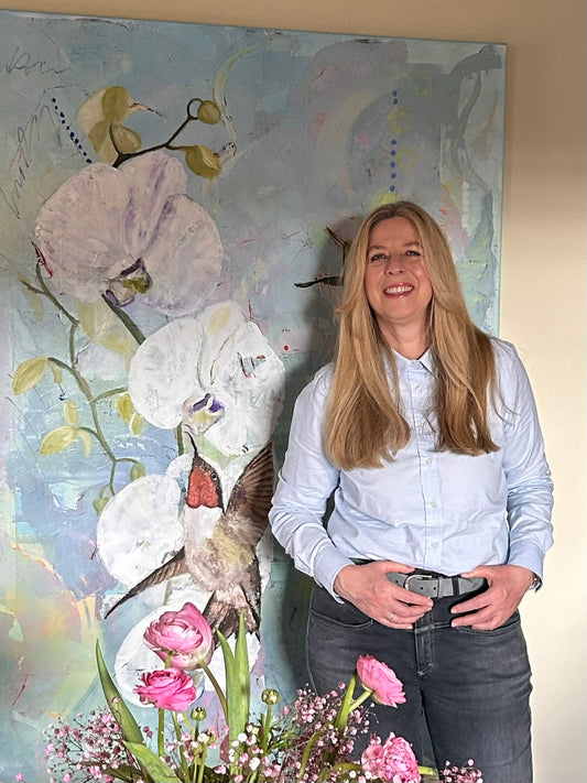 Fine Artist Andrea Ramsel in front of an oilpainting with orchids and hummingbirds 